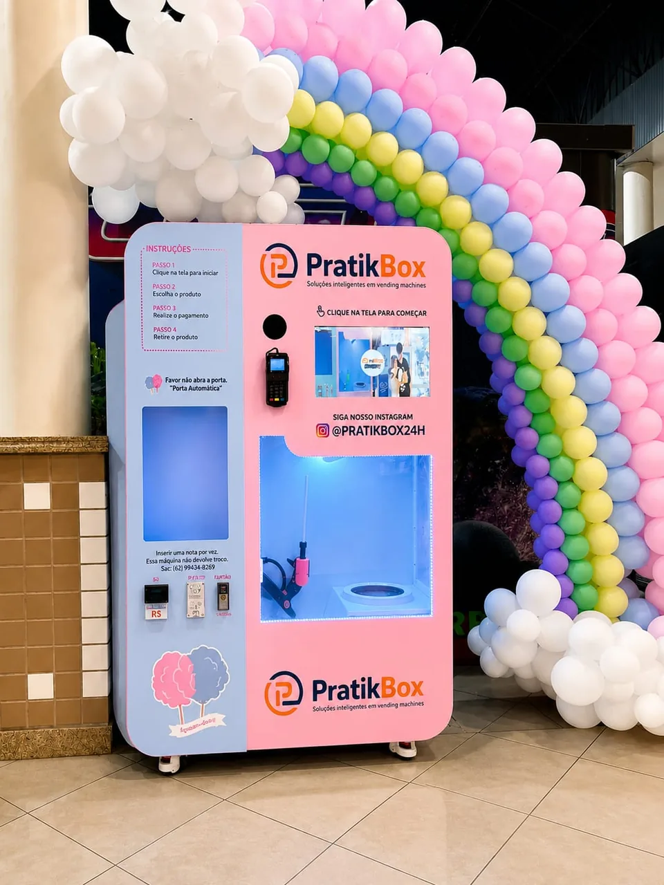 Vending machine de algodão doce PratikBox, rosa e azul, em um shopping, com arco de balões coloridos