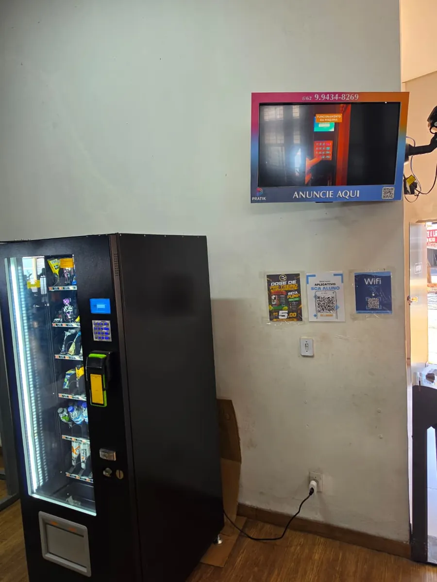 TV instalada na parede de uma sala de espera, ao lado de uma vending machine